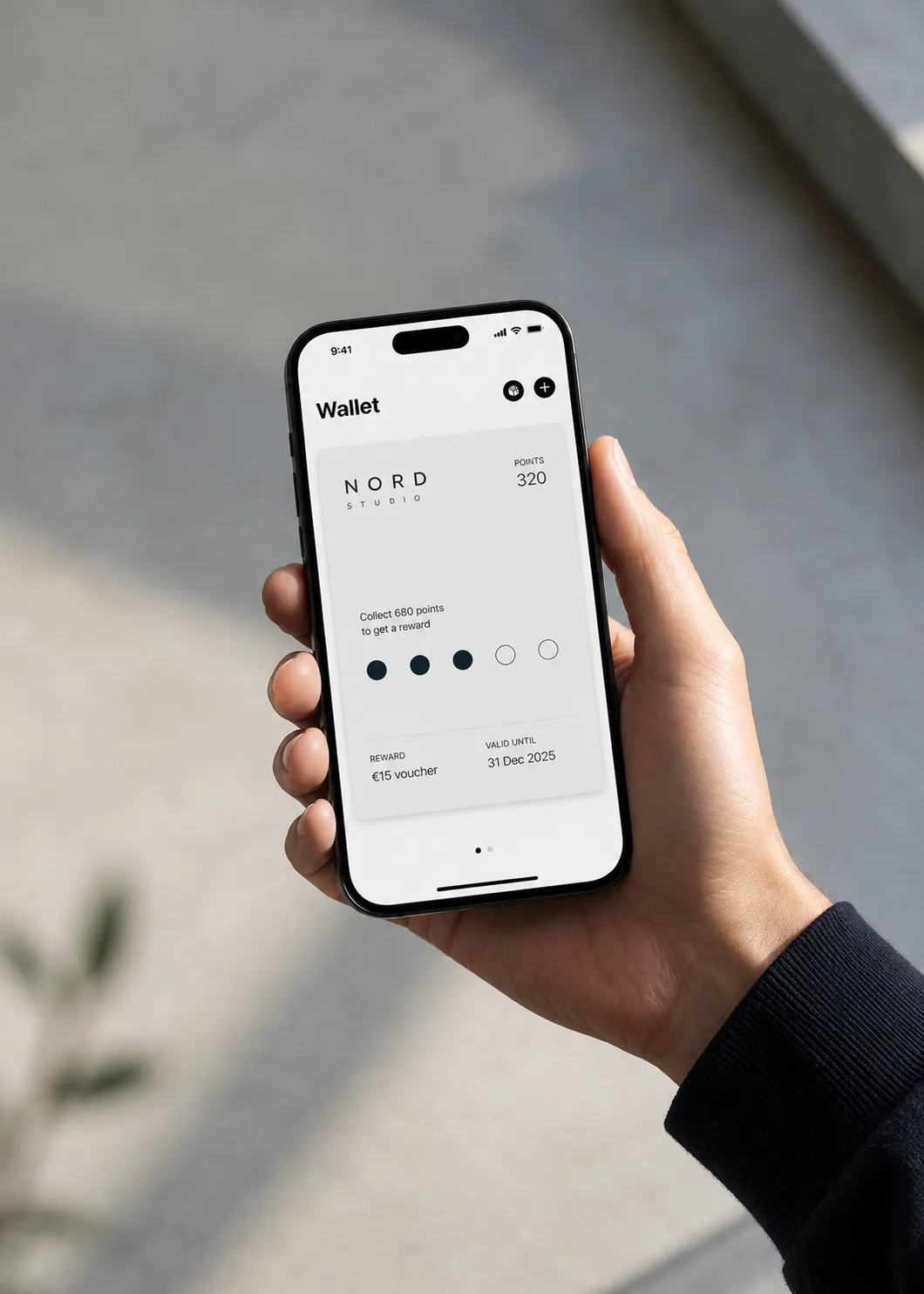 Une main tient un iPhone affichant dans Apple Wallet la carte de fidélité d’un studio, avec un compteur de points et une récompense de 15 €