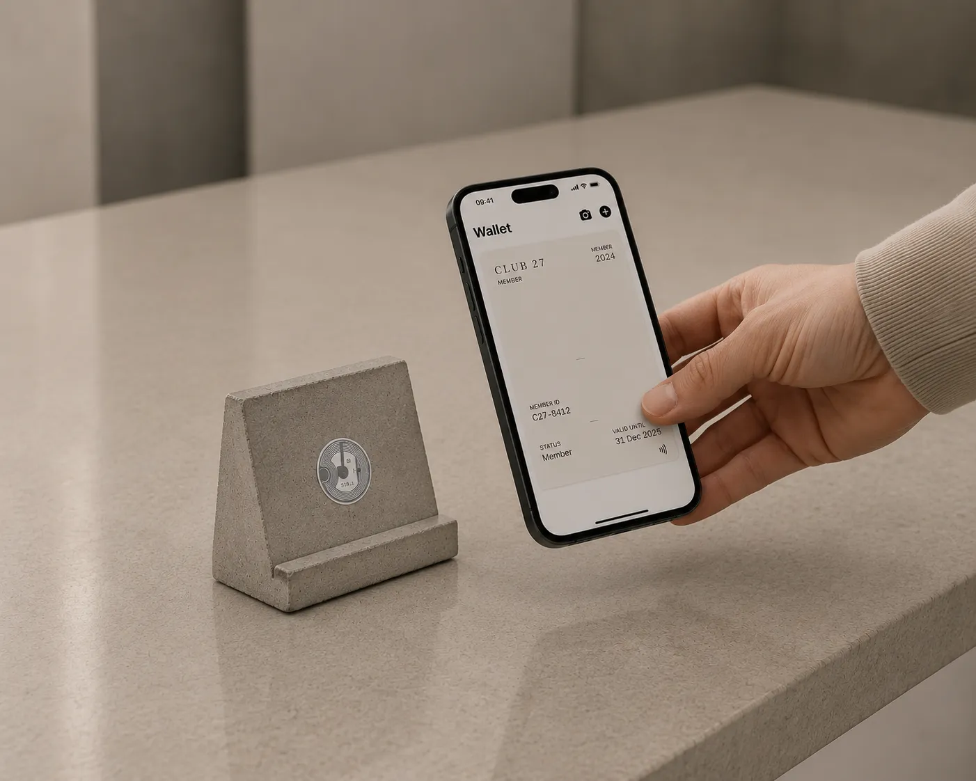 Un objet en béton posé sur un comptoir, avec une puce sans contact visible, et une main qui en approche un iPhone affichant une carte de membre dans Apple Wallet